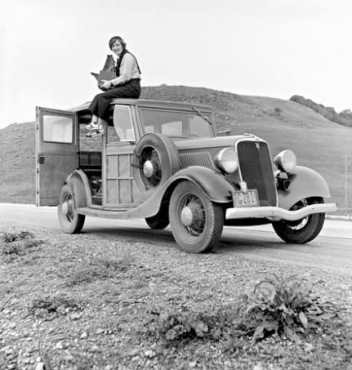 Photograph of Dorothea Lange, photographer for the Farm Security Administration (FSA), sitting on top of a 1933 Ford Model B, holding her camera, February of 1936. (This image was taken by Paul S. Taylor)