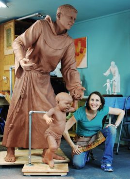 Mardie Rees stands next to the work, which was commissioned for the St. Anthony North Health Campus by the Centura Health System in Westminster, Colorado. It depicts the steadfast and wise St. Anthony guiding the young Christ Child as he takes the first steps into new discovery. In this engaging paternal moment, visitors are reminded of their own need for protection, care and comfort.