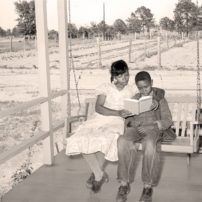 A mother reads a book to her son on the front porch swing of their home in Marshall, Texas, in April 1939. (Russell Lee/Library of Congress)