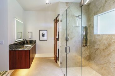 Porcelain floor tiles with zero-threshold shower and undercabinet lighting bring low maintenance, accessible and safety elements to this primary bathroom. Design by McCabe By Design LLC